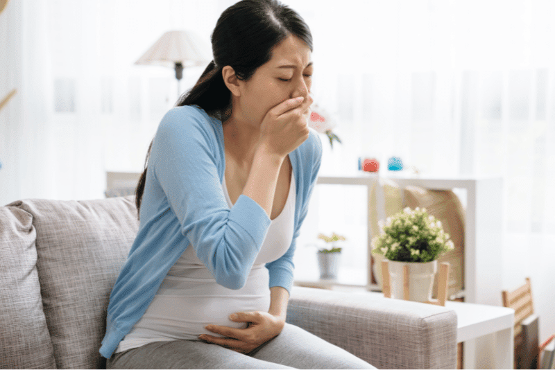 Schwangere Frau mit Übelkeit hält sich den Bauch und schaut erschöpft – Symbolbild für Schwangerschaftsübelkeit im ersten Trimester